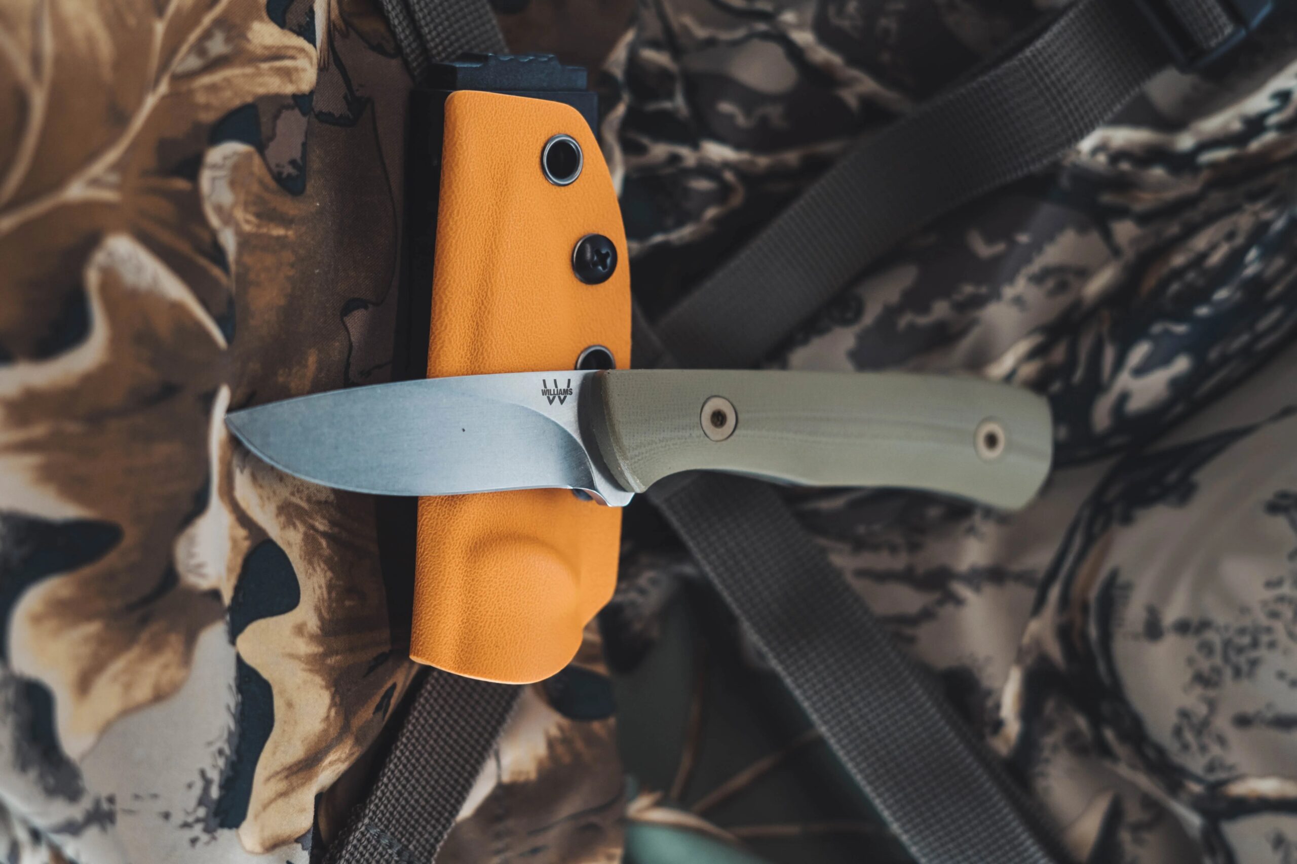 Fixed blade with a kydex sheath riding on a camouflage pack, where field maintenance actually happens