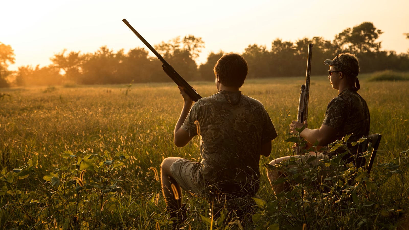 Two hunters kneeling in tall grass at first light, before the field care work starts